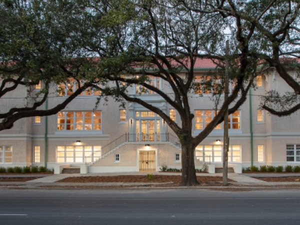 Exterior of a building at dusk with oak trees lining the sidewalk.